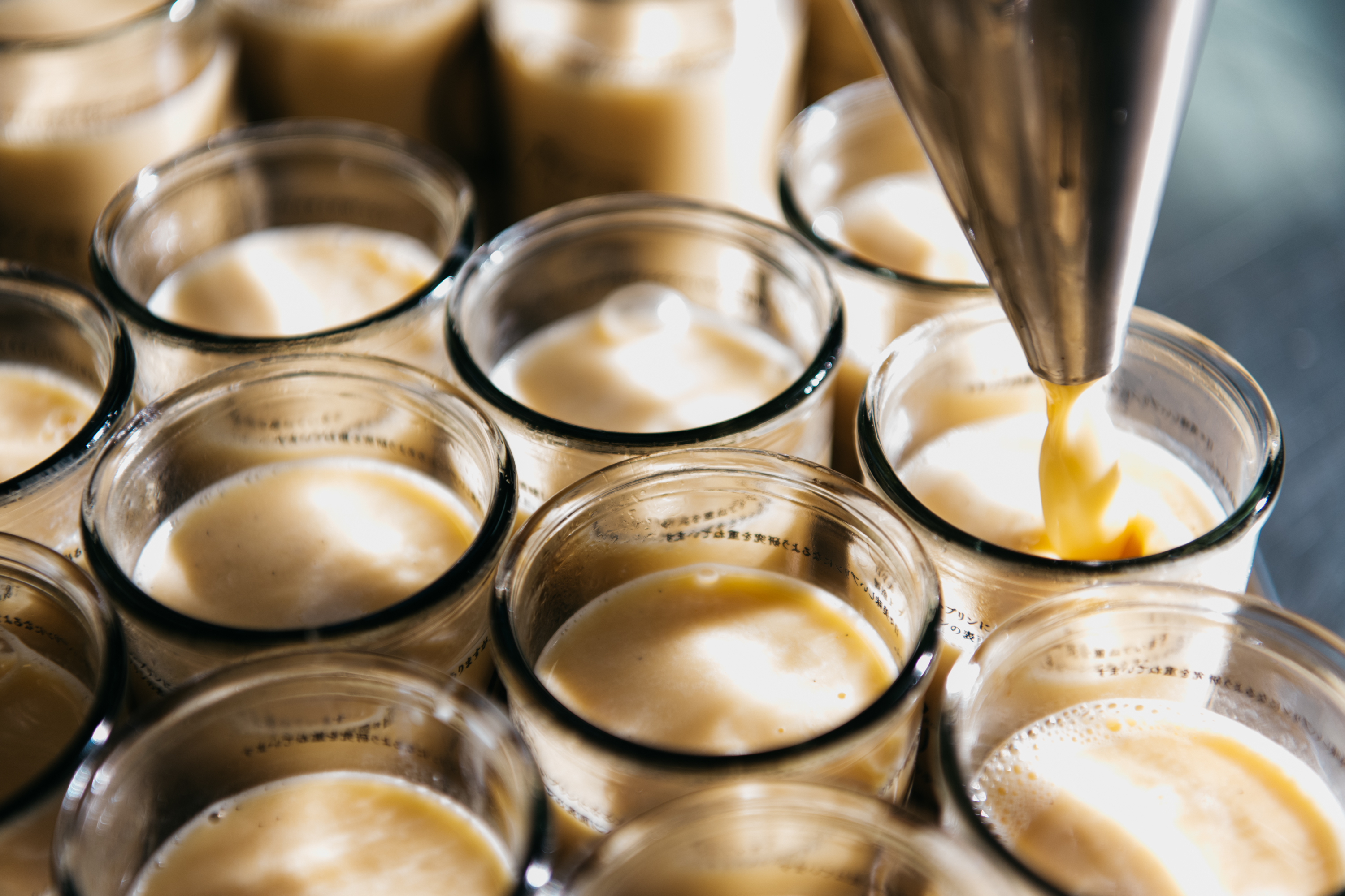 プリン本舗の製造工程 — プリン液をガラス瓶に注ぐ